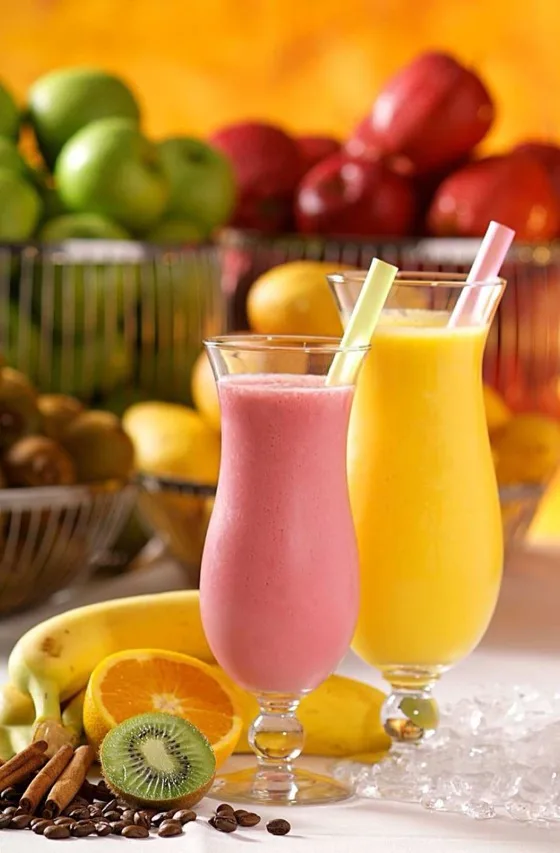 Dois copos altos de vitamina, um rosa e um amarelo, com canudos