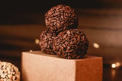Brigadeiros enrolados e cobertos de granulado, sobre suporte de madeira