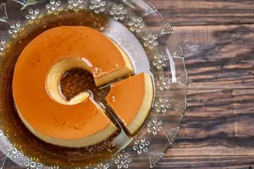 Pudim de coco dourado servido em prato de vidro sobre mesa de madeira