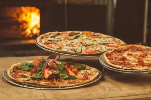 Pizza caseira redonda com cobertura de legumes, saindo do forno