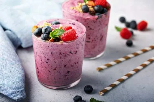 Dois copos de vitamina de frutas vermelhas com mirtilos por cima